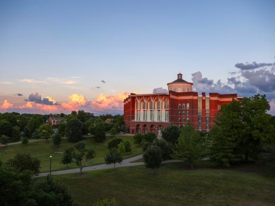Aerial view of the William T. Young Library at dusk, with trees in the foreground and clouds in the background.